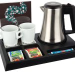 Black hospitality tray with silver kettle, 2 white mugs, spoons inside the mug. The tray shows single use fruit tea and sugar sachets. Items not included unless specified - tray only