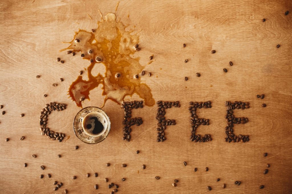 Coffee word made of coffee beans and spilled coffee from glass cup of hot espresso