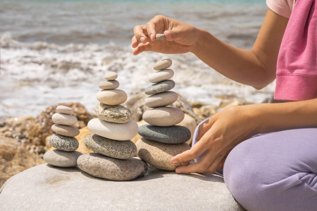 Relaxed spiritually woman hand arrangement pebble tower cobblestone sea coastline landscape closeup
